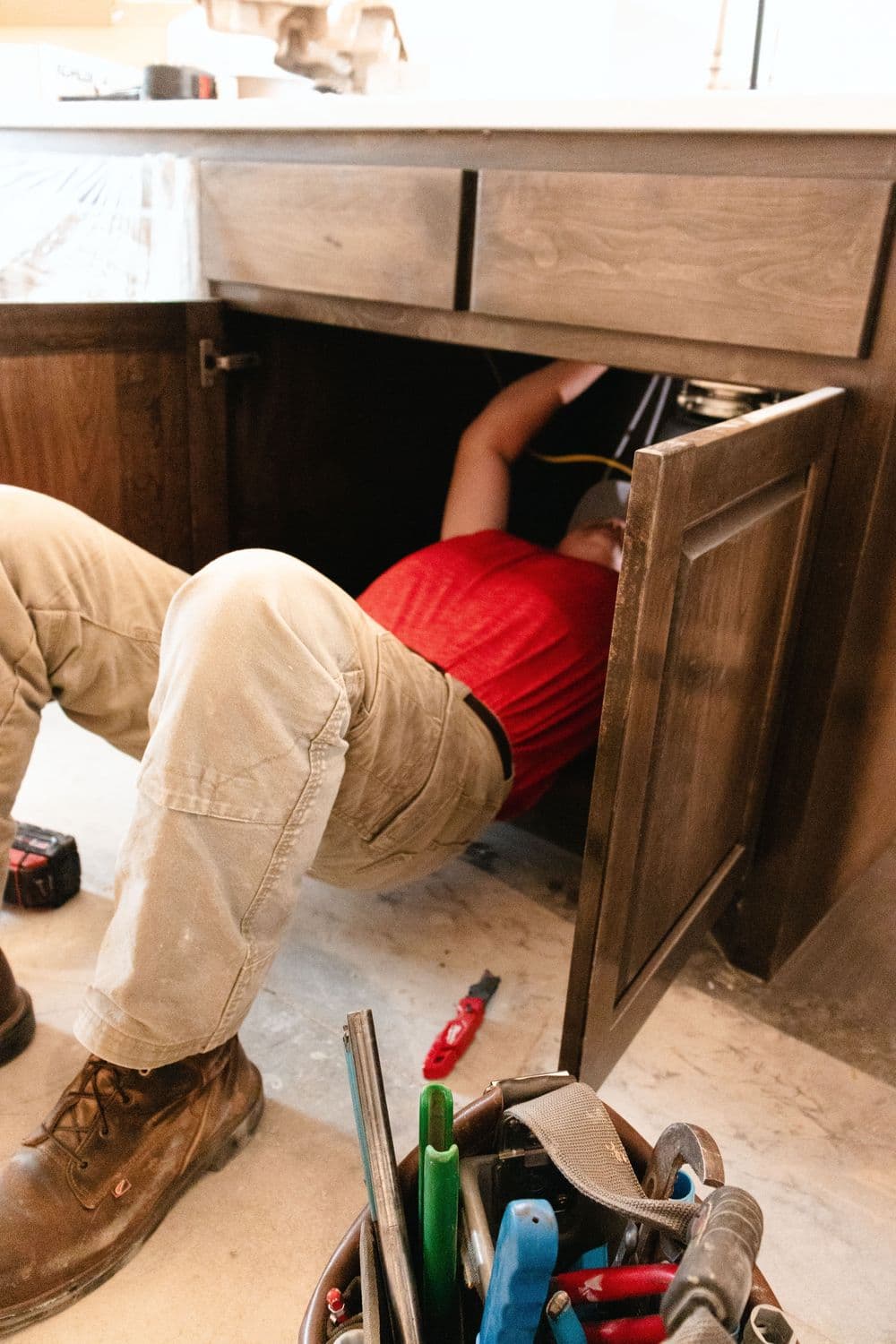 Plumber working under kitchen sink with tools nearby, showcasing home repair services.